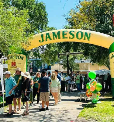 Paddy Fest St. Pete featuring green decorations, a crowd of people and Jameson whiskey blow-up bottle.