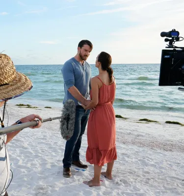 two actors hold hands on the beach while a crew films them for A Taste of Love, a Hallmark movie