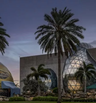 Evening outside photo of the Dali Museum in St. Pete featuring palm trees, the Dali 360 dome and the front of the museum.
