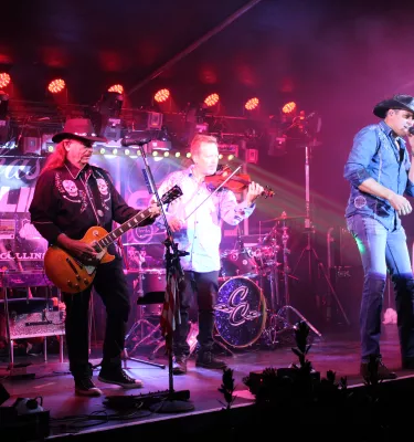 Country tribute band on a stage performing music with pink lighting.