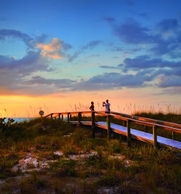a couple on a boardwalk over the dunes at Pass-a-Grille Beach at sunset