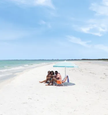 a mom, dad and little girl sit under a beach umbrella at Fort De Soto Park's beautiful white-sand beach