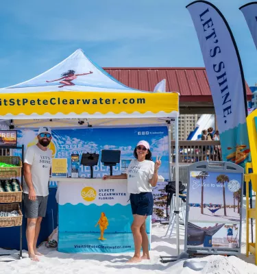 two smiling people stand under at tent for Visit St. Pete/Clearwater to answer questions