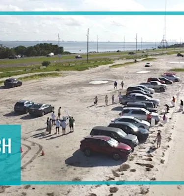 Aerial shot of multiple cars parked on a beach with volunteers cleaning up.