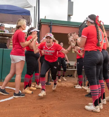 Girls softball team in red uniforms high-fiving on the field.