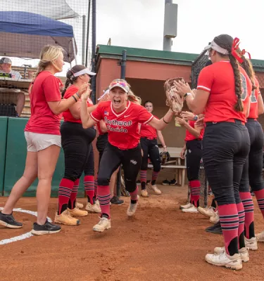 Girls softball team in red uniforms high-fiving on the field.