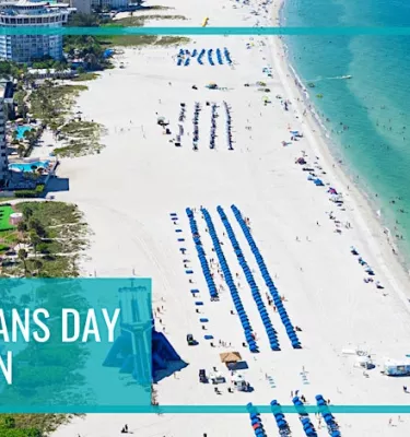 Aerial photo of a beach strip featuring multiple blue cabanas and a city skyline.