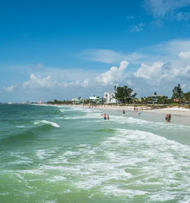 the surf rolls up on a white beach where there are swimmers and walkers