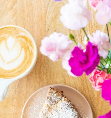 latte in a ceramic mug with a pastry and bright pink flowers