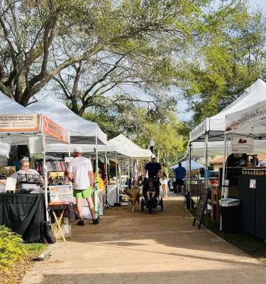 People walking at an outside market featuring many white vendor tents.
