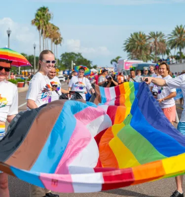 people in rainbow colored clothing carrying a pride flag in a parade