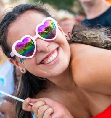 LGBTQ+ parade visitor holding a rainbow flag and smiling at the camera.