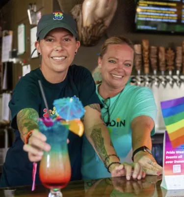 Dunedin Pride Ladies Luau event photo featuring two bartenders serving a colorful pride drink.