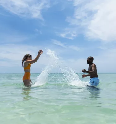 a couple splashes playfully in calm green gulf waters at the beach