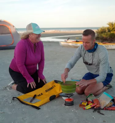 man and woman cooking food on the beach