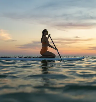 a woman kneeling on a paddleboard at sunset