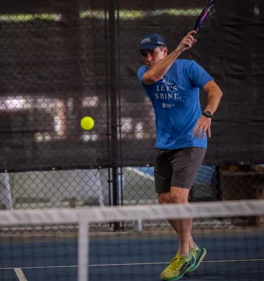a man in a blue shirt and hat playing pickleball