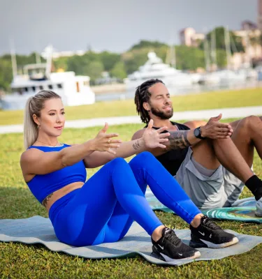 2 pilates instructors teaching a mat pilates class outside on the grass.