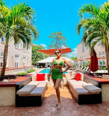 Una mujer con un traje de baño verde brillante posando frente a bancos y una piscina cerca de palmeras en el Hotel Fenway