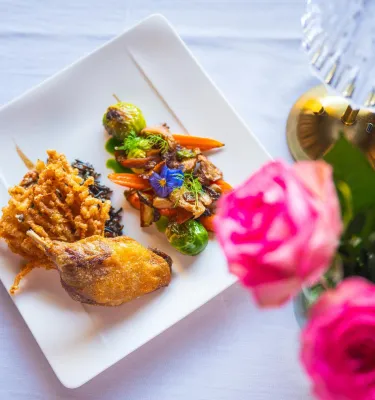 A view of a beautifully plated dish at Black Pearl Restaurant in Dunedin, accompanied by bright pink roses on the white linen tablecloth