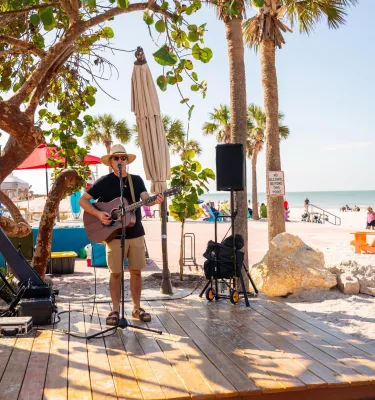 a person in a tshirt and hat playing guitar on a wooden deck at Paradise Grille on Pass-a-Grille Beach