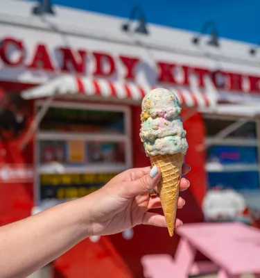 a person's hand holding a stacked ice cream cone in front of the nostalgic red and white Candy Kitchen in Madeira Beach