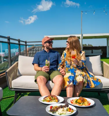 man and woman sitting on outdoor couch looking at each other enjoying drinks on rooftop