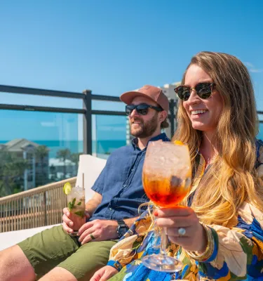 woman and man holding cocktails sitting outside on rooftop smiling