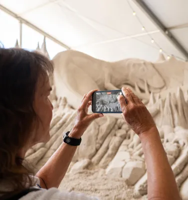 A woman taking a photo of a sand sculpture