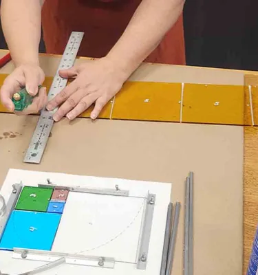 Art class featuring hands using a measuring stick and pencils.