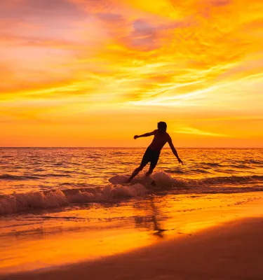 a young man rides a skimboard at sunset on Treasure Island Beach