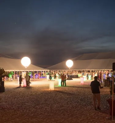 Evening sunset luau event on the beach featuring white tents and floating lanterns.