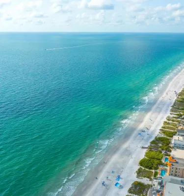 aerial view of Indian Rocks Beach lined with a strip of white sand beach and blue-green waters; hotels and condo buildings line the shore