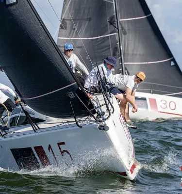 Multiple men driving a sailboat in the water.