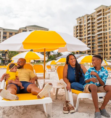 a family relaxes in lounge chairs on the beach at Sandpearl Resort