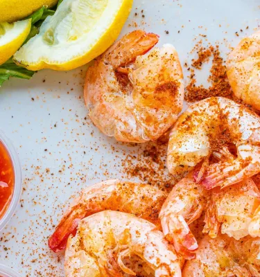 steamed shrimp sprinkled with bay seasoning, next to cocktail sauce and lemon slices