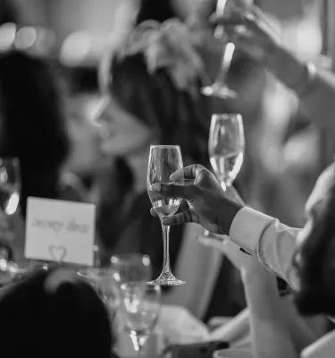 Black and white photo of people at tables toasting with champagne. 