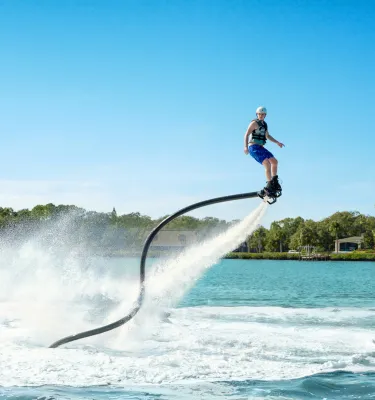 a person on a flyboard who is airborn, with water jets streaming behind them