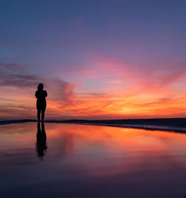 a woman stands on the beach and watches a brilliant sunset in St. Pete-Clearwater