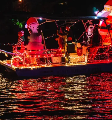a small boat decorated with holiday lights and blow-up holiday decorations of Santa and a snowman