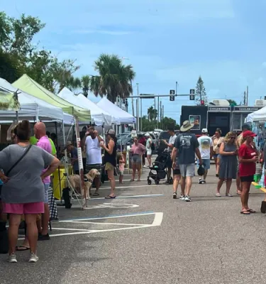 People at an outdoor market shopping around various white tents.