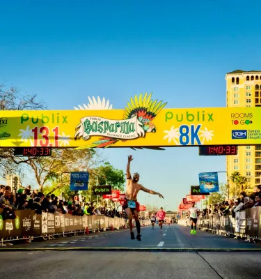 a happy runner crosses the finish line at Gasparilla Distance Classic