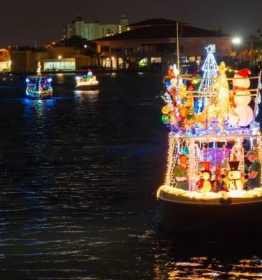 Holiday boat parade featuring decorated boats sailing on the water at night.