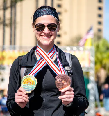 a smiling woman displaying two medals from the St. Petersburg Distance Classic