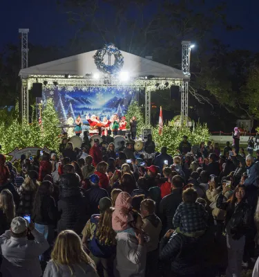 Outdoor nightly Winter Wonderland holiday festival featuring a stage with people watching a show.