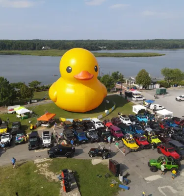 Big yellow duck statue with jeeps parked around it.