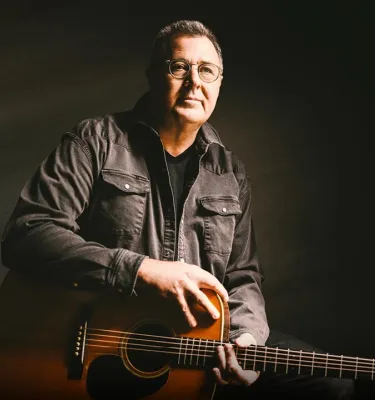 Musician Vince Gill holding an acoustic guitar.