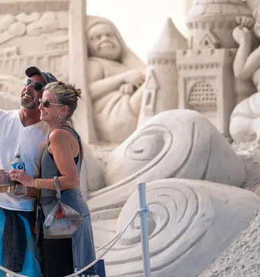 a couple taking a selfie in front of a giant sand sculpture at the Pier 60 Sugar Sand Festival