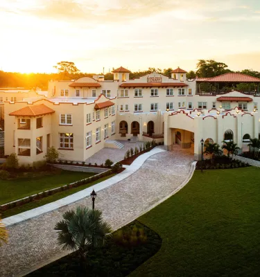 Exterior photo of a white hotel with a sunset in the background.