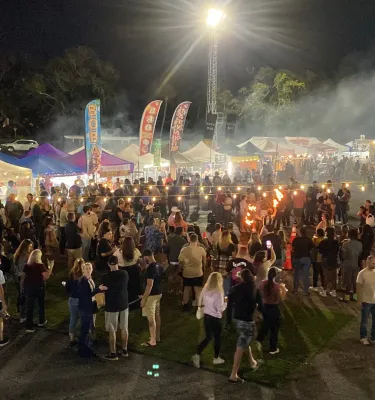 Outdoor evening market featuring a crowd of people with surrounding vendor tents.